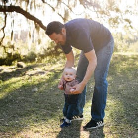 dad walking with baby in natural light in front of big tree