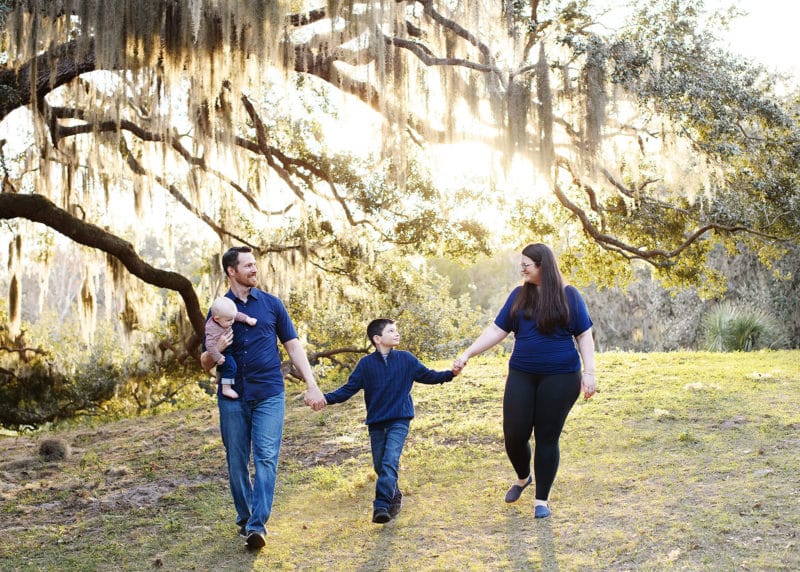 family of four holding hands walking together in front of a big tree in tampa florida