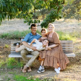 family of four hugging on the park bench in davis california