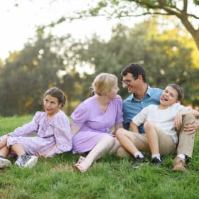 young family of four sitting in the grass with goofy faces in the park davis california