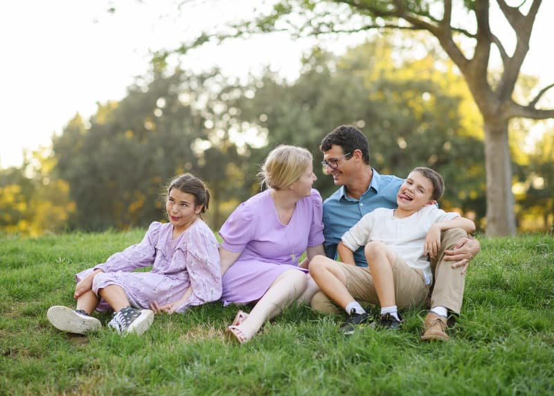 young family of four sitting in the grass with goofy faces in the park davis california