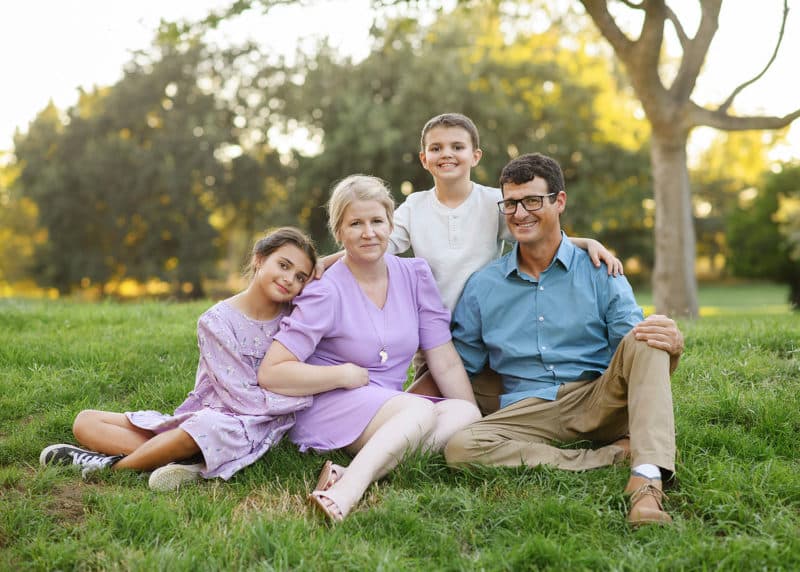 young family sitting on the grass under a tree during summer in davis california