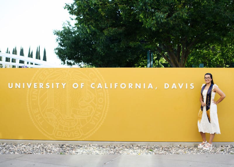 graduation pictures in front of yellow UC Davis sign in a white dress