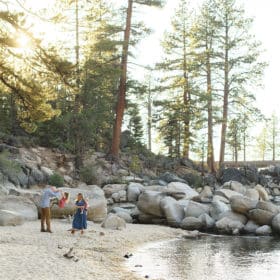 family of four walking along the beach at lake tahoe with pine trees and boulders