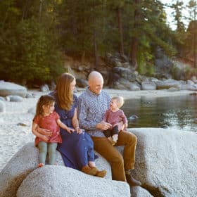 mom and dad with two young girls sitting on the rocks at lake tahoe beach