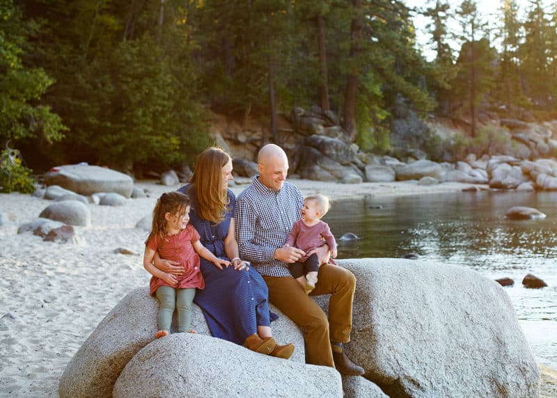 mom and dad with two young girls sitting on the rocks at lake tahoe beach