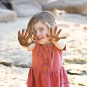 toddler girl holding out sandy hands on the beach at lake tahoe