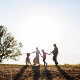 family of four holding hands together walking the sunset silhouette