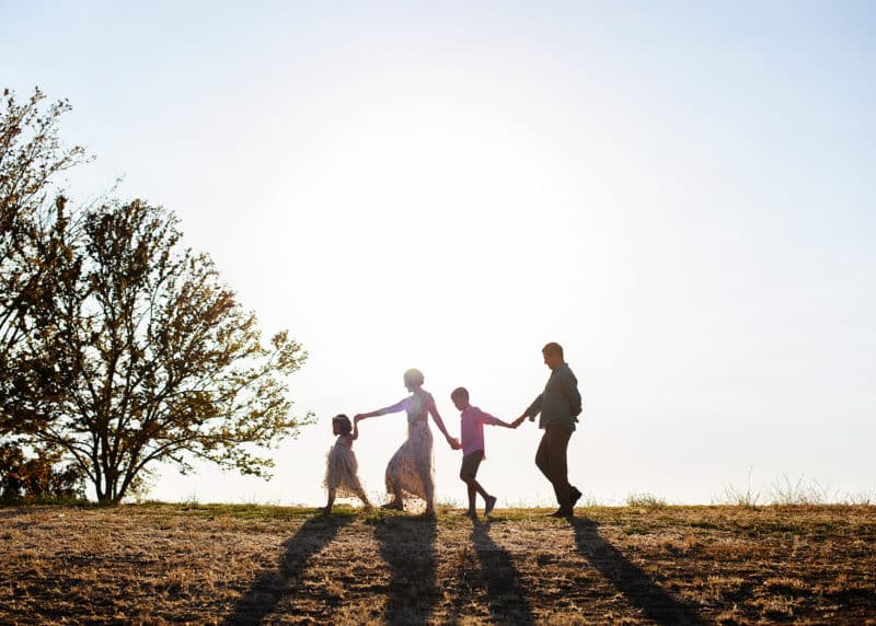 family of four holding hands together walking the sunset silhouette