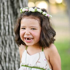 little girl wearing a flower crown laughing outside with missing front teeth