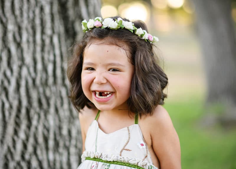 little girl wearing a flower crown laughing outside with missing front teeth