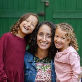 mom with two young girls standing in front of a green door during fall family photos