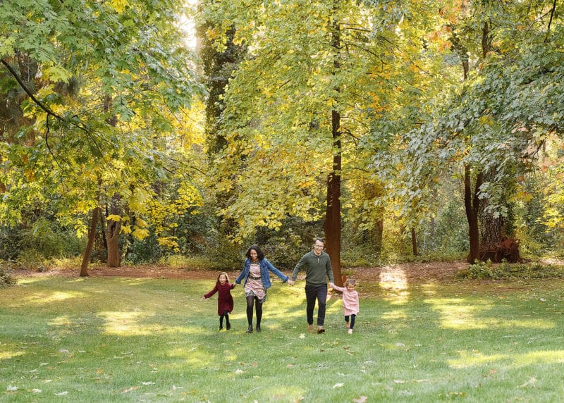 family of four linking hands walking forward in front of a forest of trees