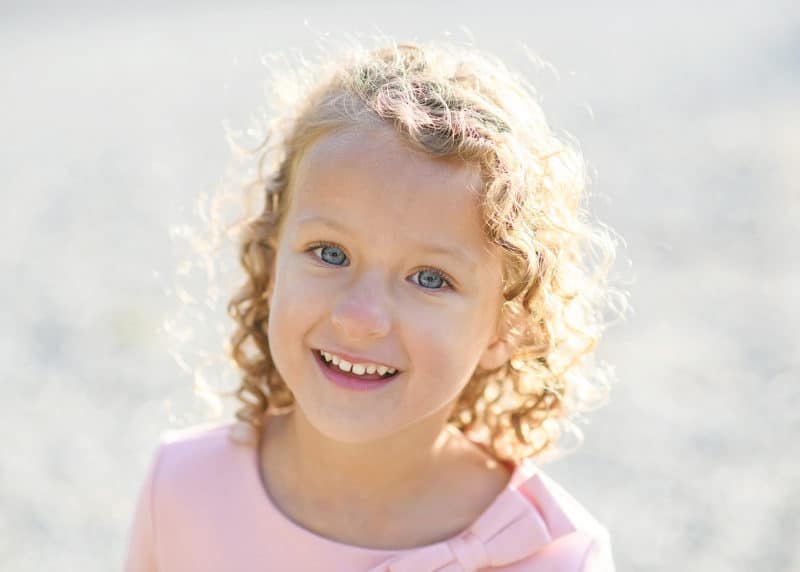 young girl with curly hair and a pink dress smiling during family photos in empire mine california