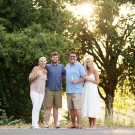 Family of four posing in the shade of oak trees holding wine glasses