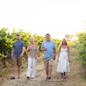 family of four walking through a vineyard in the summer light with wine glasses