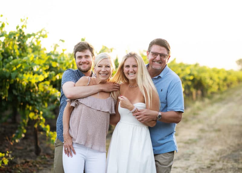 family of four laughing together in a vineyard in the summer sunset california