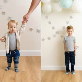 one year old boy holding hands with dad, big brother standing against wall