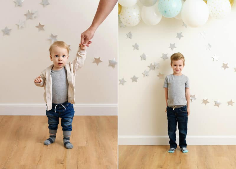 one year old boy holding hands with dad, big brother standing against wall