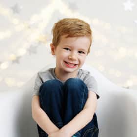 young boy sitting in a chair smiling with lights behind him