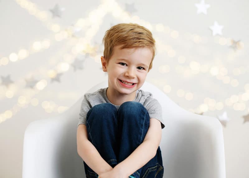 young boy sitting in a chair smiling with lights behind him 