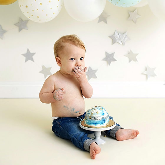 young boy licking his hands during a one year old cake smash shoot in the studio