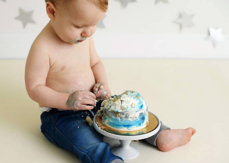 young boy looking at his one year old smash cake digging his hand into it