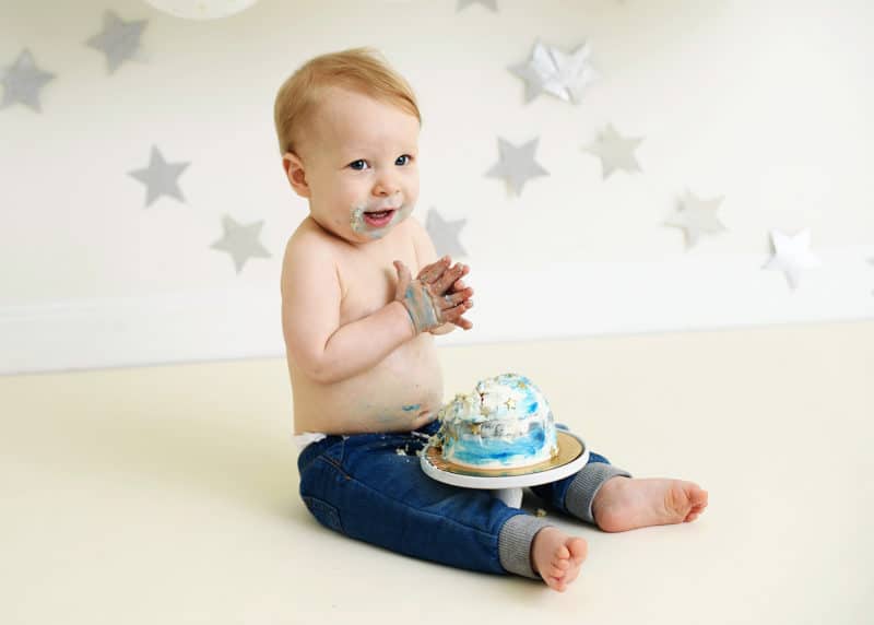 baby boy digging into his smash cake clapping hands in a studio shoot