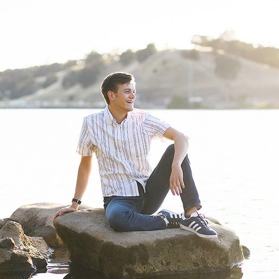high school senior sitting on a rock in folsom lake during photo session