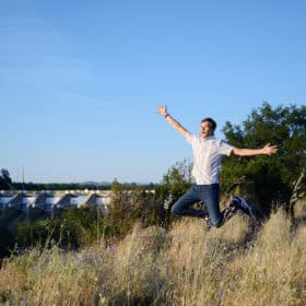 high school senior boy jumping with arms raised in front of folsom dam california