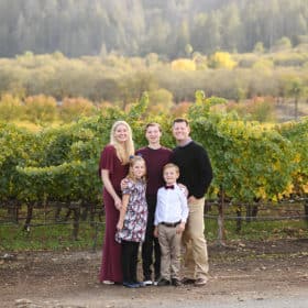 family of five standing outside a vineyard during fall season in napa california