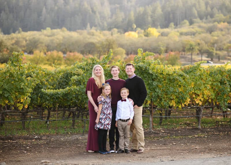 family of five standing outside a vineyard during fall season in napa california