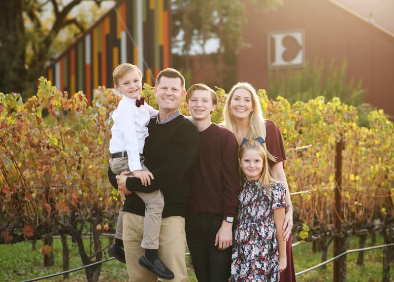 family of five posing together in front of family vineyard and wine tasting area in napa california