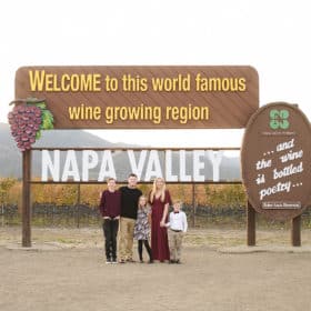 family of five standing in front of sign that says “welcome to this world famous wine growing region, Napa Valley”