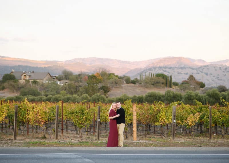 couple posing in front of family vineyard with scenic napa valley mountains in the background