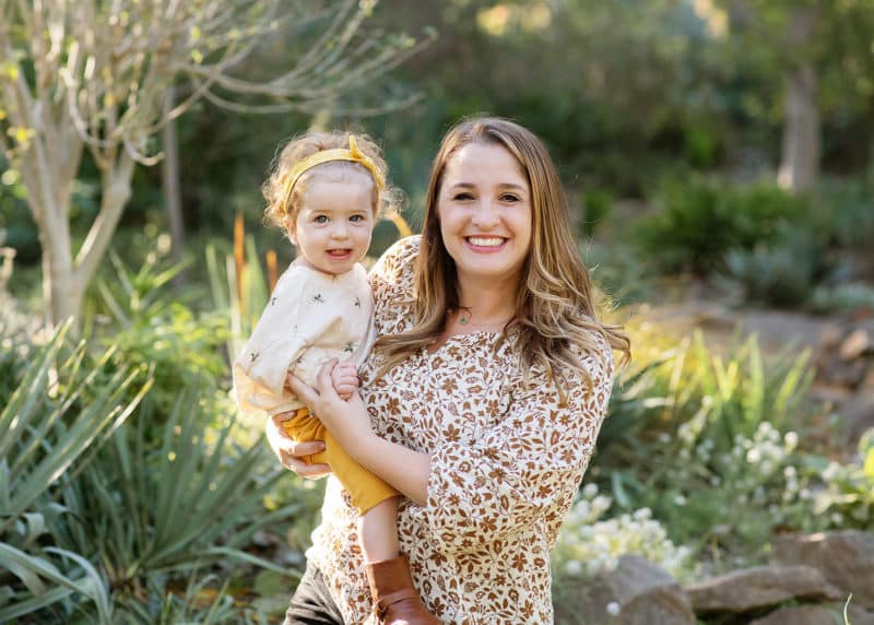 mom holding young daughter and smiling in front of a succulent garden in sacramento california