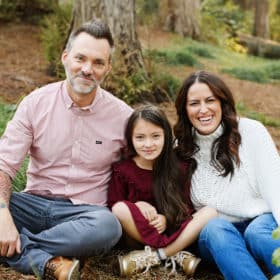 mom dad and young daughter sitting on the forest floor during fall family photo shoot