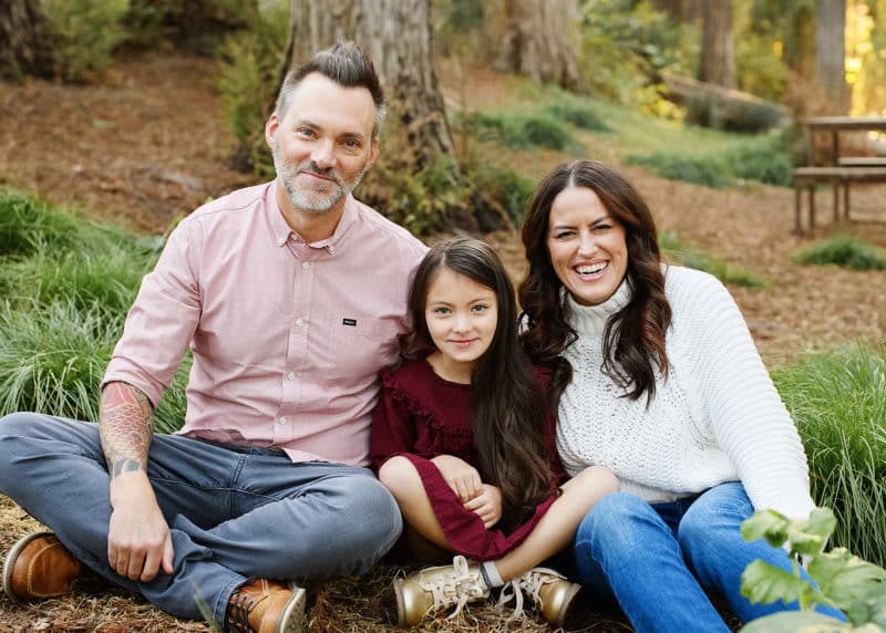 mom dad and young daughter sitting on the forest floor during fall family photo shoot