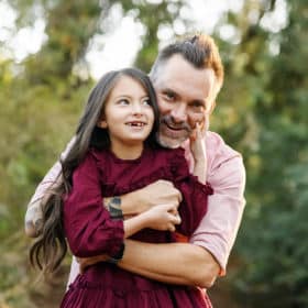 dad hugging young daughter from behind and smiling during fall family photos