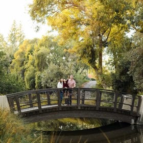 family of three standing on a bridge in the middle of the trees in davis california