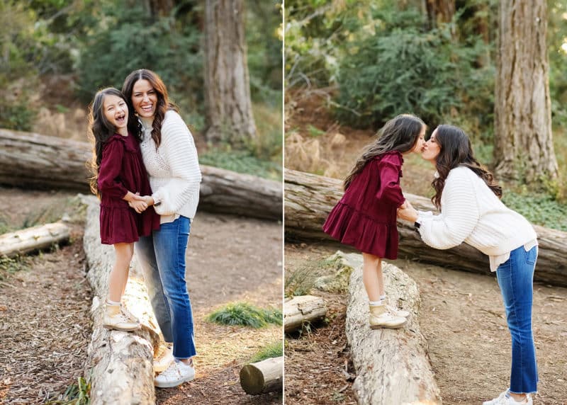 Mom with young daughter walking along a log in the forest in davis california