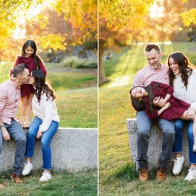 family of three taking pictures during fall with yellow leaves, mom and dad kissing and laughing