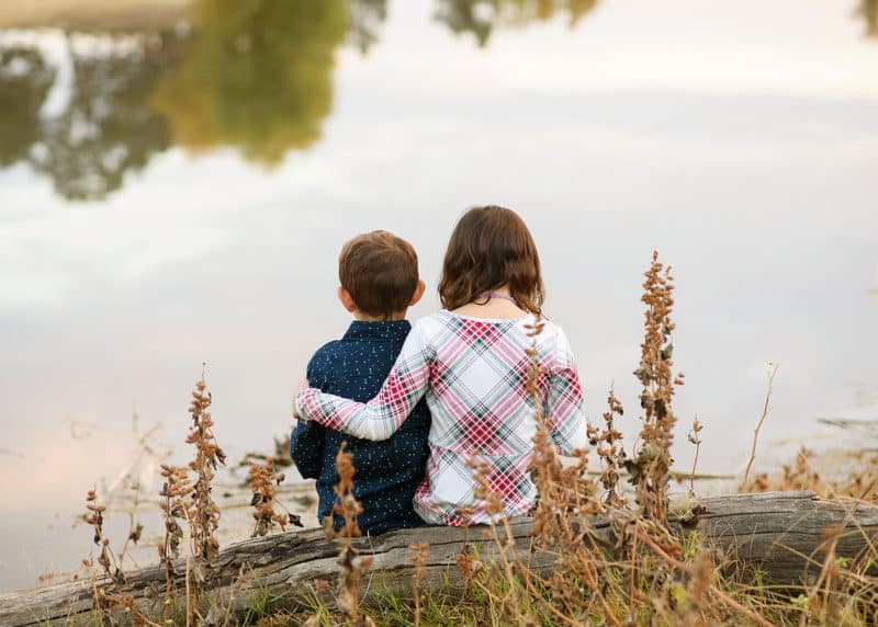 young brother and sister sitting together by the water during a cloudy fall day in sacramento california