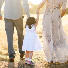 young girl holding hands with mom and dad walking through a field in folsom california
