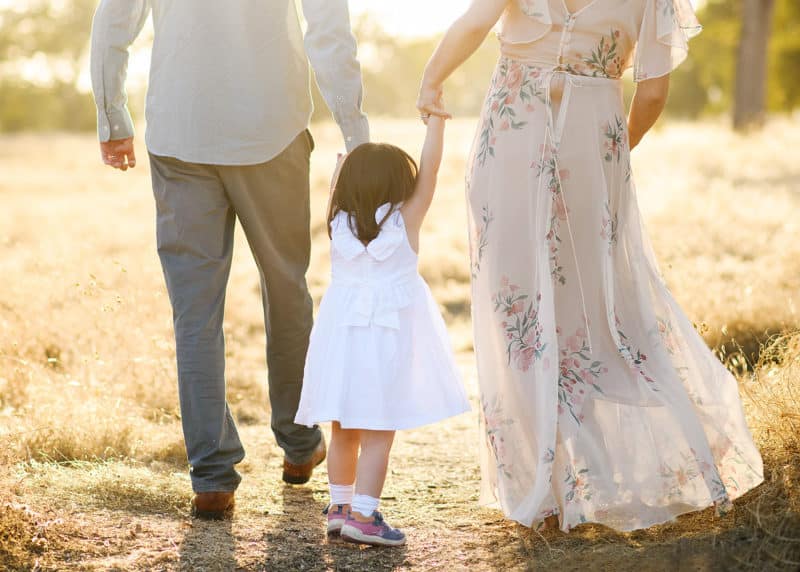 young girl holding hands with mom and dad walking through a field in folsom california