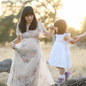 young girl walking on a log while holding hands with dad and pregnant mom in folsom california