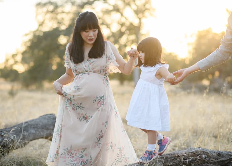 young girl walking on a log while holding hands with dad and pregnant mom in folsom california