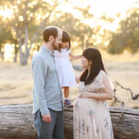 man and pregnant woman holding young daughter while standing on a log in family photo session in folsom california