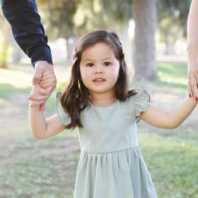 little girl holding hands with mom and dad looking at the camera during family photo shoot