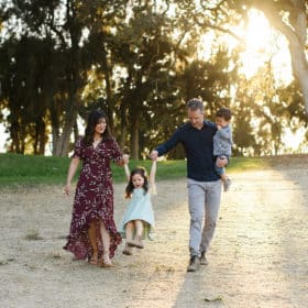 mom and dad with two young kids walking along the grass during golden hour in sacramento california